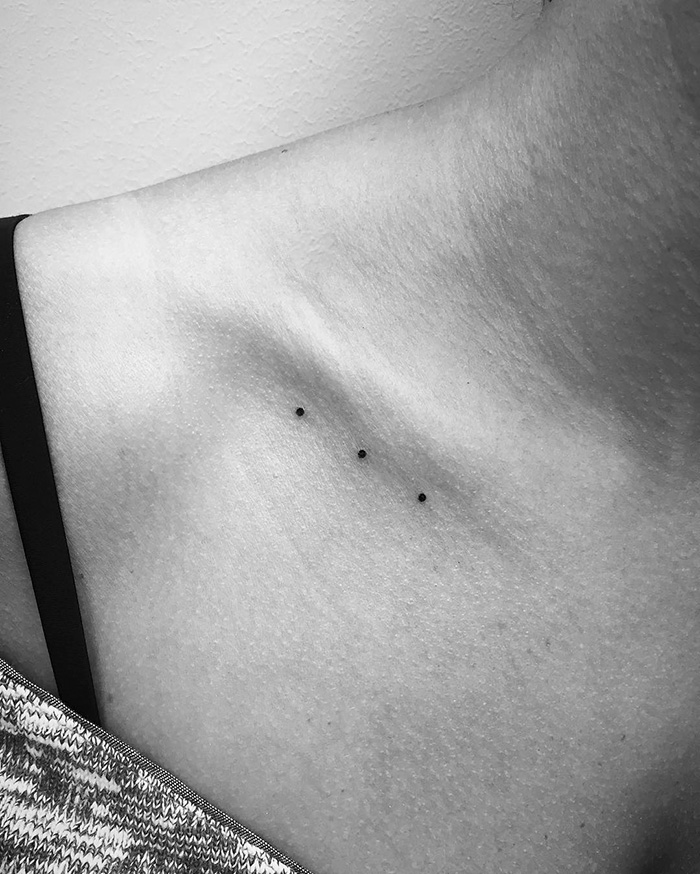 Minimalist digital tattoo of three small dots on a woman's collarbone.