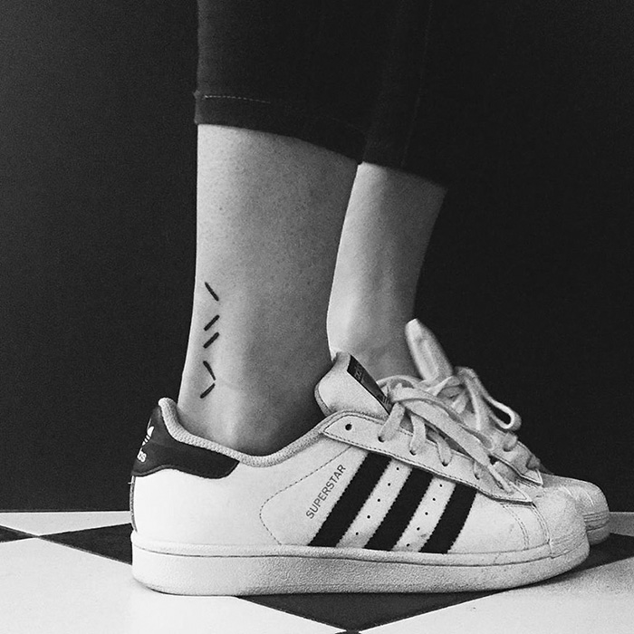 Minimalist digitally-designed tattoo on ankle, wearing Adidas sneakers.