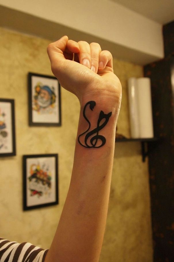 Cat tattoo with musical note design on a wrist, showcasing unique cat person expression.