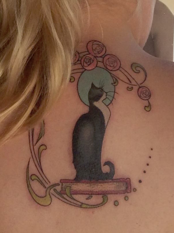 Cat tattoo design featuring a black cat silhouette with decorative floral elements on a person's upper back.