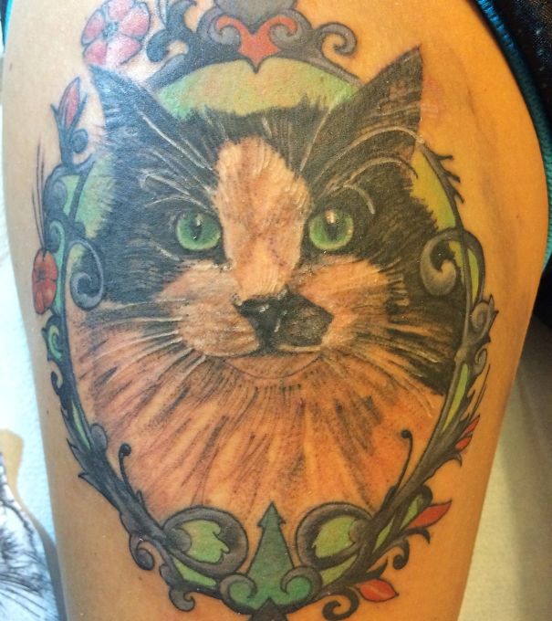 Colorful cat tattoo with intricate floral design framing the feline face.