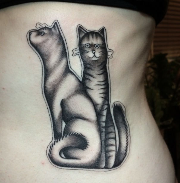 Cat tattoo depicting two stylized feline figures on a person's side.