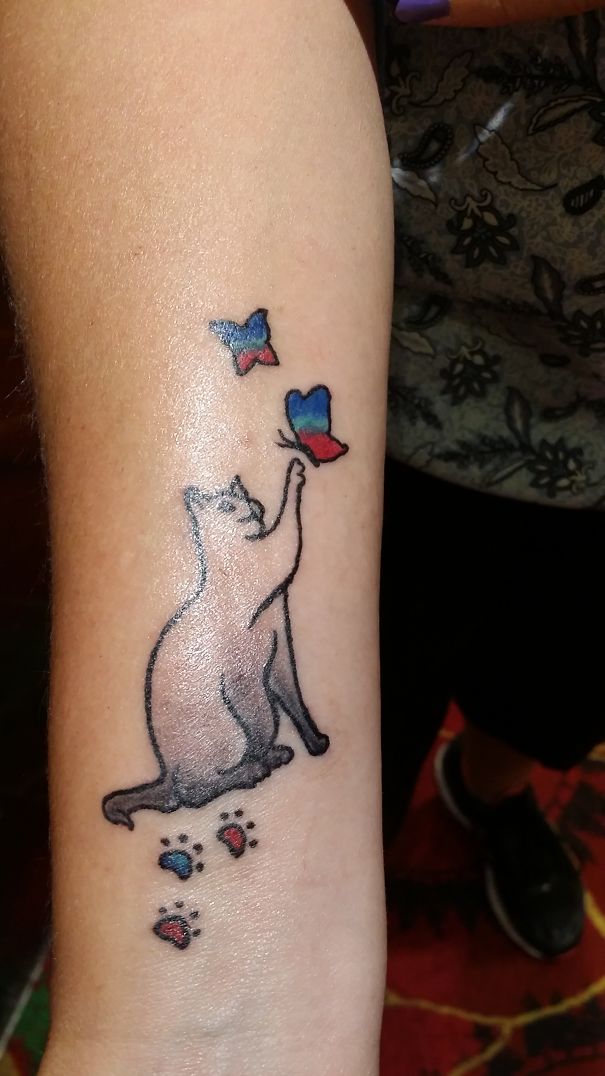 Cat tattoo with butterflies and paw prints on a forearm.