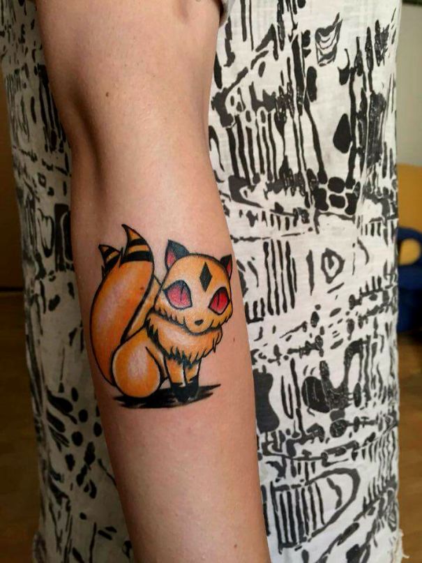 Orange cat tattoo on forearm, featuring bold outlines and red eyes.