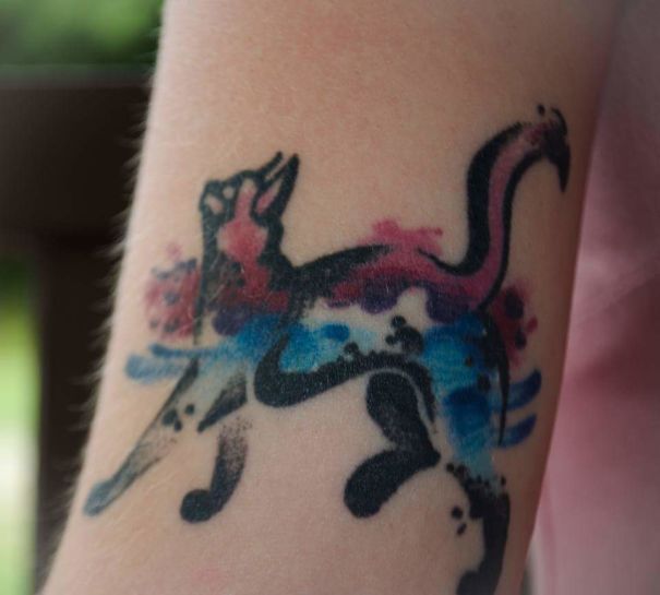 Watercolor cat tattoo in abstract style on forearm, featuring vibrant pink and blue hues for cat tattoo enthusiasts.