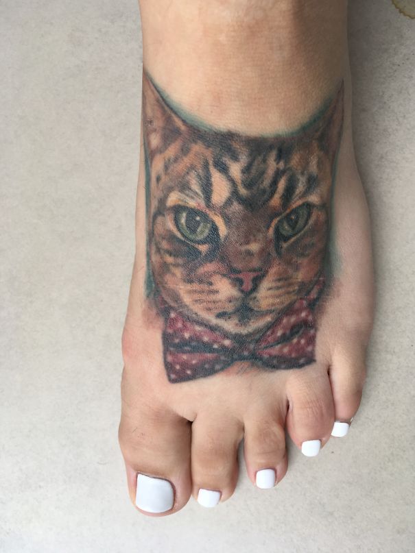 Cat tattoo on a foot, featuring a detailed feline face with a bow tie.
