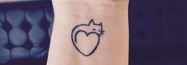 Minimalist cat tattoo in the shape of a heart on a person's wrist, perfect for cat lovers.