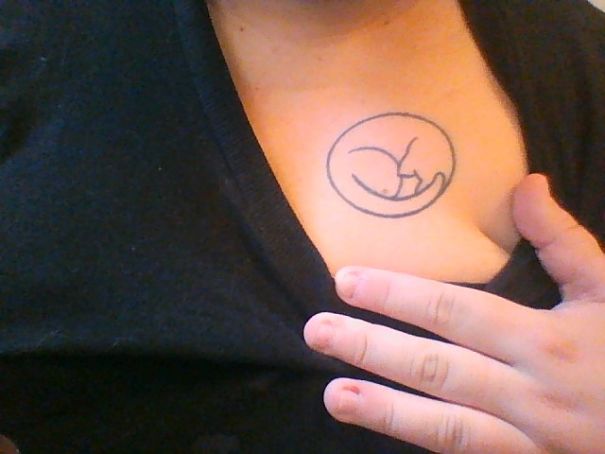 Minimalist cat tattoo on a person's chest, showcasing a simple outline design.