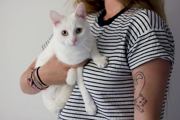 Person holding a white cat with a cat tattoo on their arm, expressing love for cats.