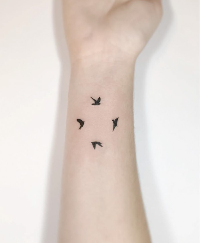 Small bird tattoos on a wrist, showcasing elegant minimalist design.