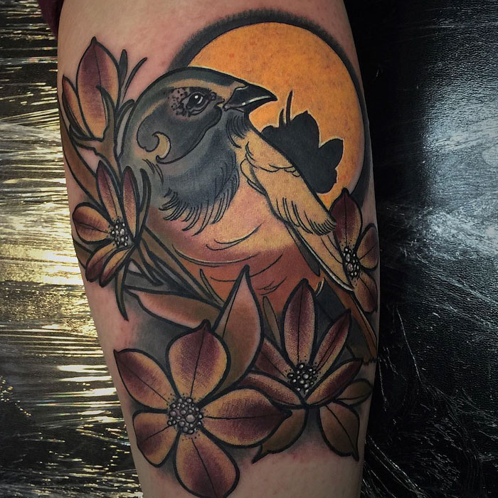 Small bird tattoo featuring floral elements and a sunset background.