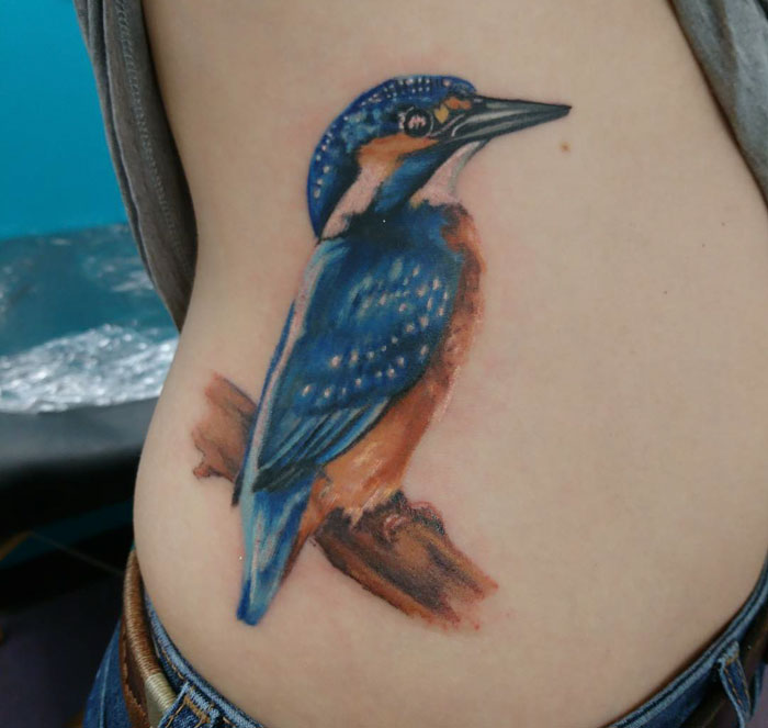 Colorful small bird tattoo of a kingfisher perched on a branch.