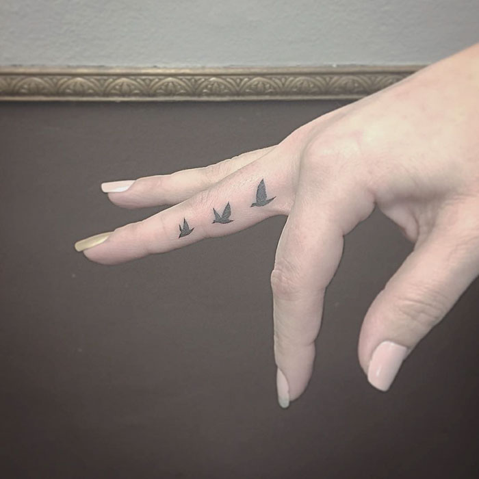 Small bird tattoos on a finger, featuring three flying silhouettes for a unique design.