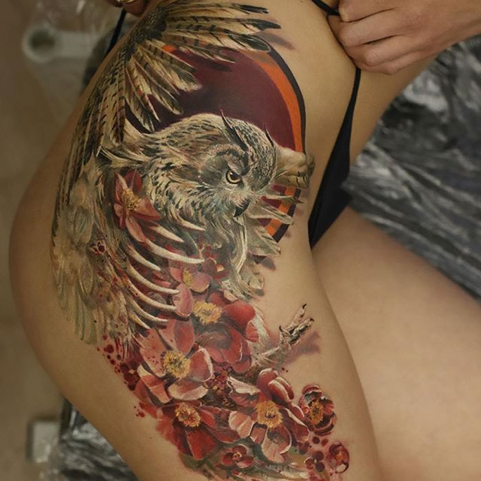 Close-up of a detailed small bird tattoo with floral elements on the thigh.