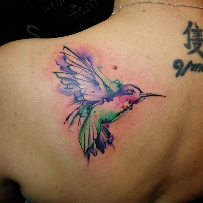 Watercolor small bird tattoo on shoulder, featuring vibrant colors and intricate design.