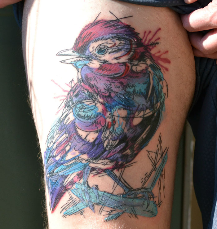 Colorful small bird tattoo with abstract style on an upper arm, showcasing unique ink patterns.