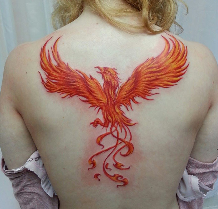 Vibrant phoenix tattoo on a person's back, showcasing unique small bird art.