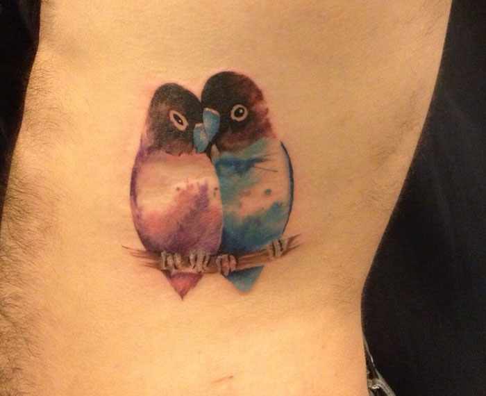 Colorful small bird tattoo featuring two birds perched together.