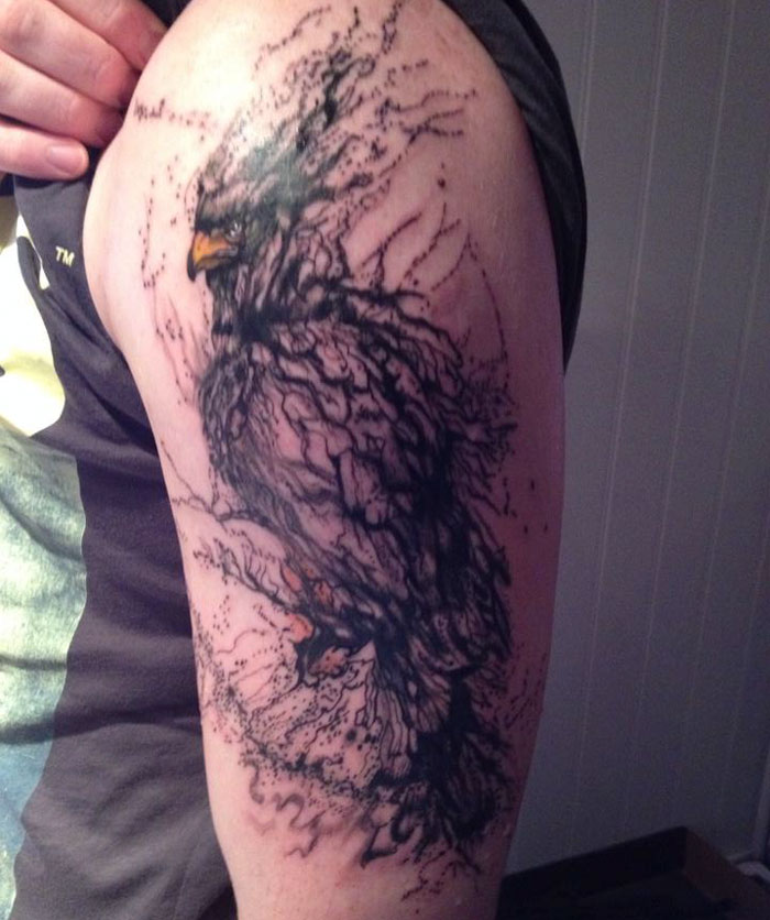 Unique small bird tattoo with intricate, abstract design on a person's upper arm.