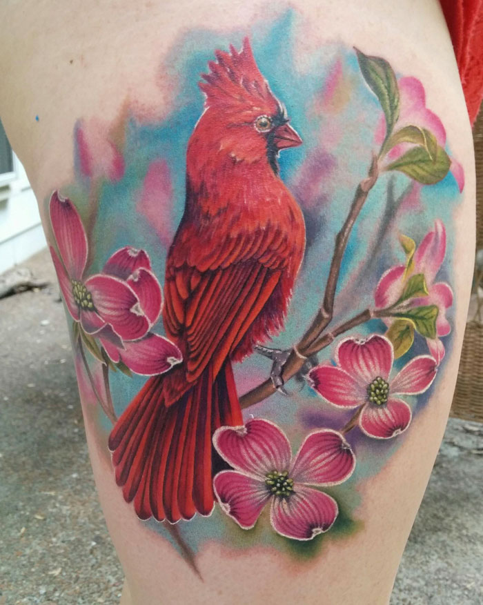 Unique small bird tattoo of a colorful red cardinal perched on a flowering branch with vibrant blossoms.