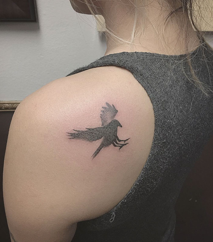 Small bird tattoo on person's shoulder, featuring a black silhouette design.