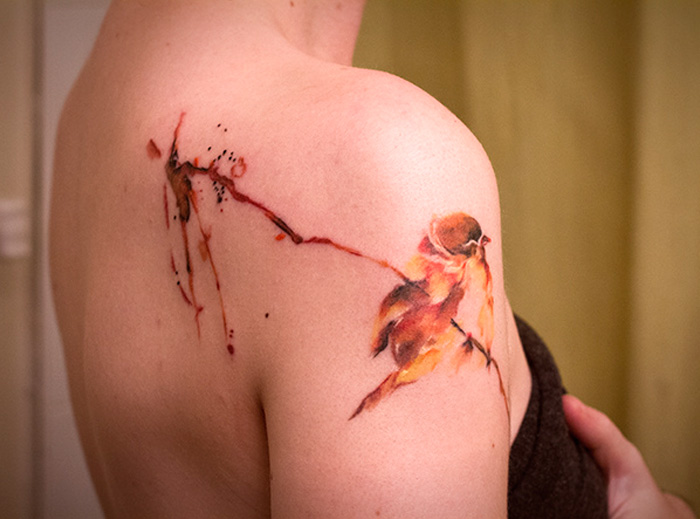 Small bird tattoo on shoulder with watercolor design.