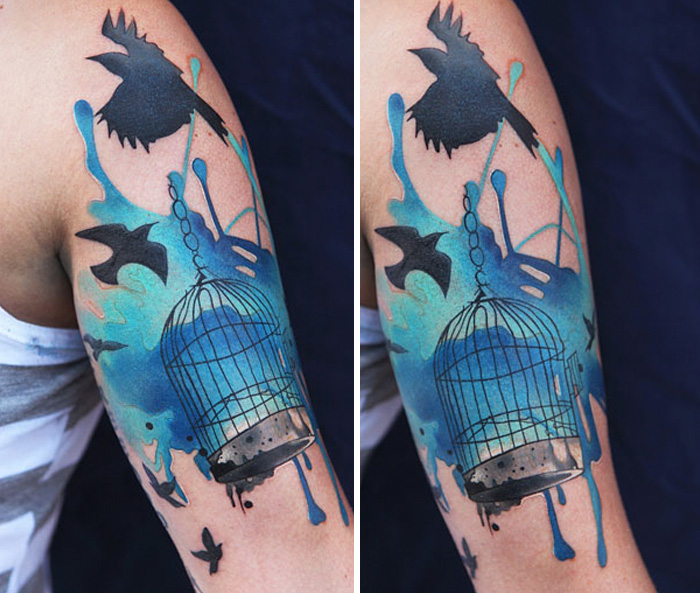 Unique small bird tattoo with blue watercolor splashes and black birds around a cage on an arm.