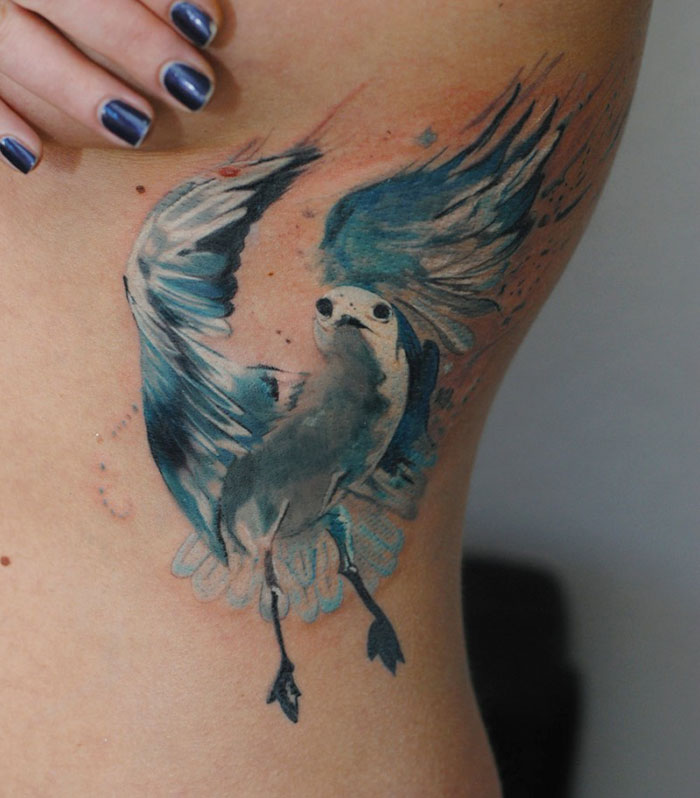 Small bird tattoo inked in vibrant blues on side of a person's body.