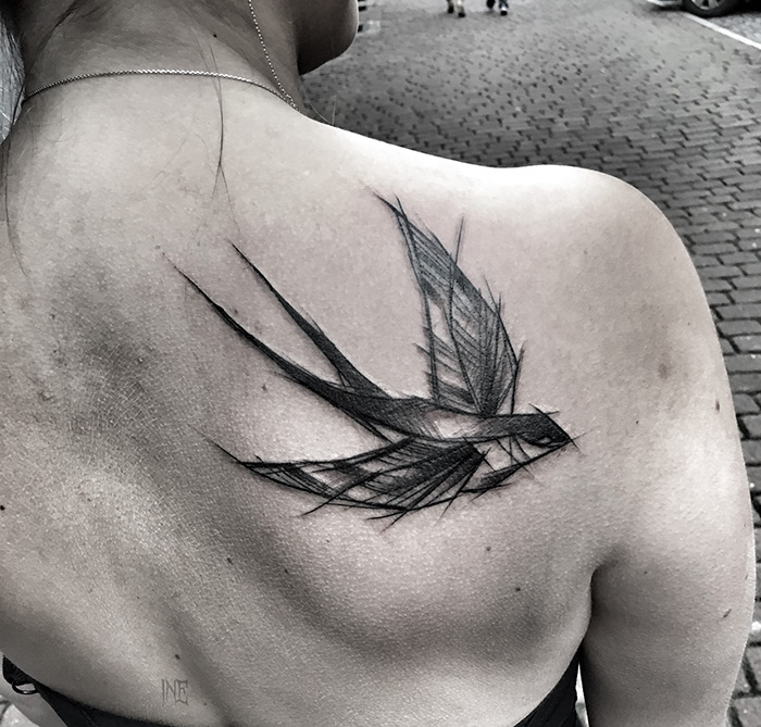 Minimalist small bird tattoo on a woman's shoulder, showcasing unique design with artistic flair.