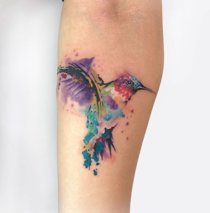 Colorful small bird tattoo with watercolor effect on forearm.
