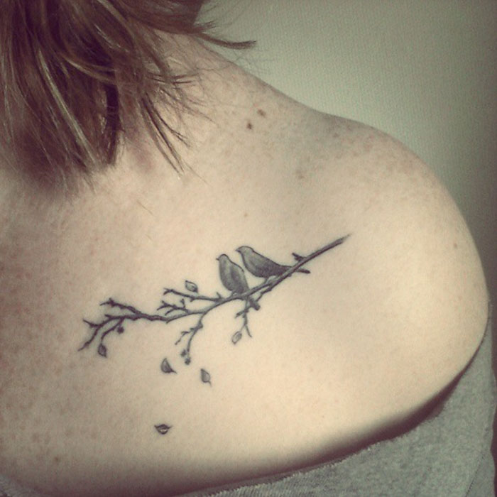 Small bird tattoo on shoulder featuring two birds perched on a branch, elegantly designed for artistic inspiration.
