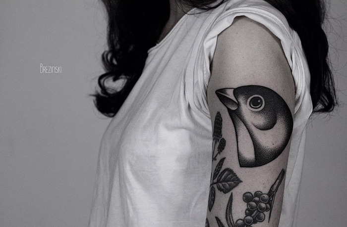 Woman with a unique small bird tattoo on her upper arm, featuring intricate details and shading.