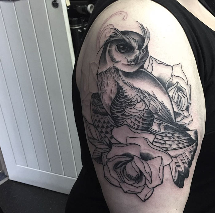 Unique small bird tattoo featuring an owl surrounded by roses on an upper arm.
