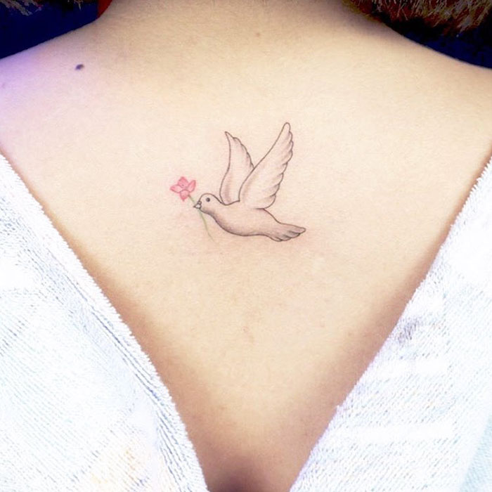 Small bird tattoo with a flower on a person's upper back, showcasing delicate ink art design.