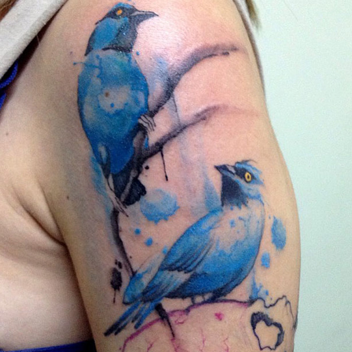 Colorful small bird tattoos on arm with blue ink detailing.