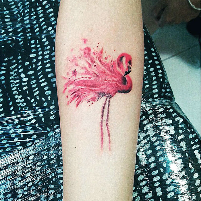 Small bird tattoo featuring a vibrant pink flamingo on an arm, showcasing unique artistic detail.