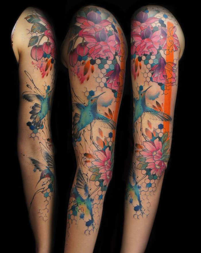 Colorful small bird tattoos on arm with floral and geometric designs.