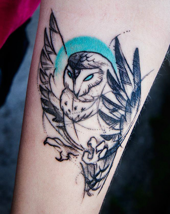 Abstract small bird tattoo design on forearm with vibrant blue accents.