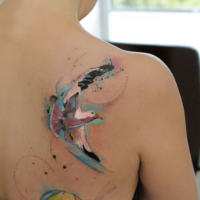 Watercolor small bird tattoo on shoulder, vibrant colors, unique design.