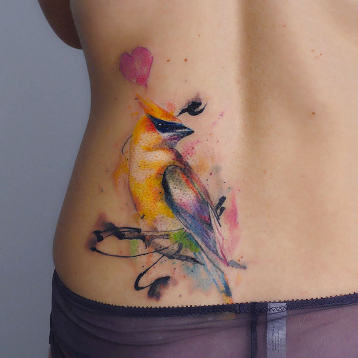 Colorful small bird tattoo on hip with heart detail, showcasing unique inkspiration.