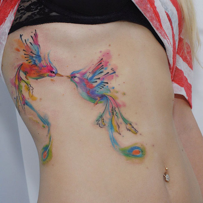 Colorful small bird tattoos on a person's side, showcasing artistic watercolor style.