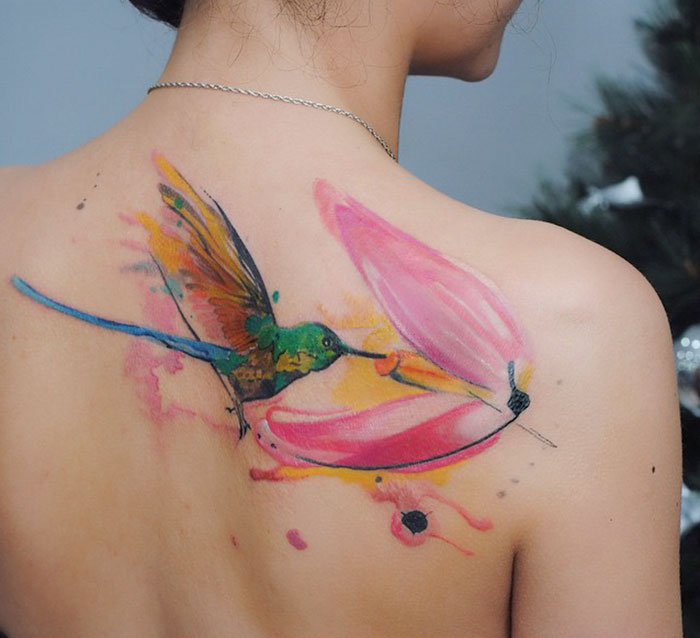 Colorful small bird tattoo with floral design on upper back.