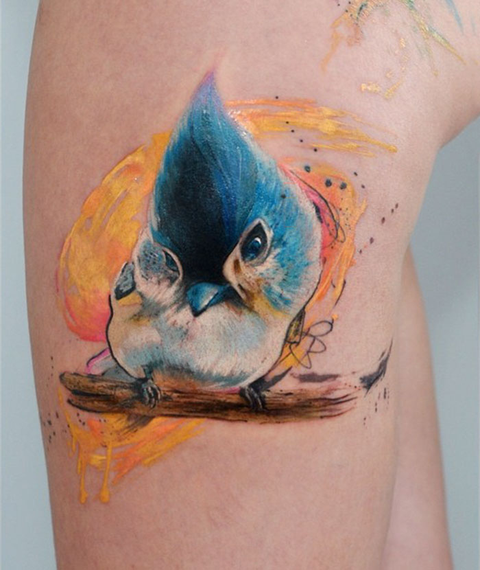 Colorful small bird tattoo featuring a vibrant blue and orange design on the skin.