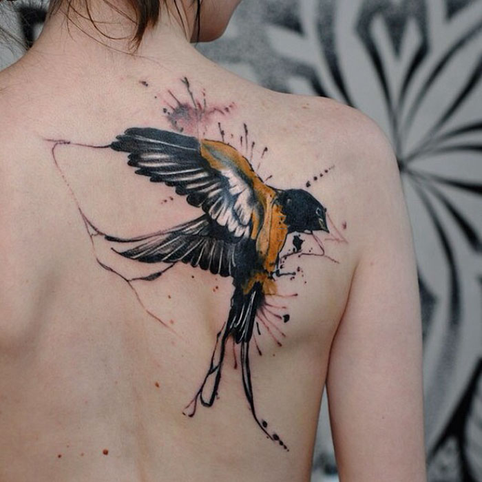 Unique small bird tattoo on shoulder, vibrant watercolor style.