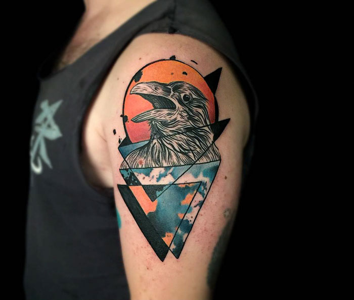 Small bird tattoo with geometric design and sunset background on upper arm.