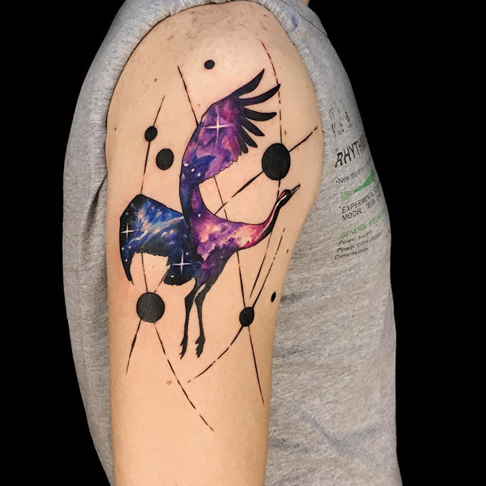 Cosmic small bird tattoo with purple galaxy design on upper arm.