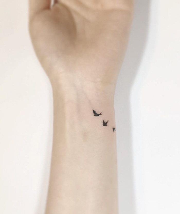 Minimalist small bird tattoos on a wrist, showcasing delicate black ink design.