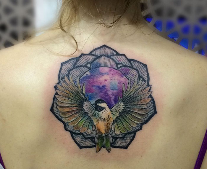 Colorful small bird tattoo on back with geometric patterns.