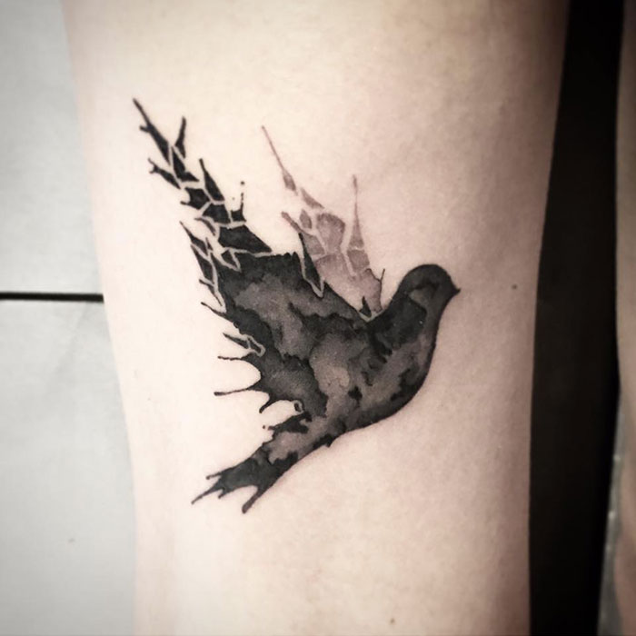 Unique small bird tattoo with artistic black shading on skin.