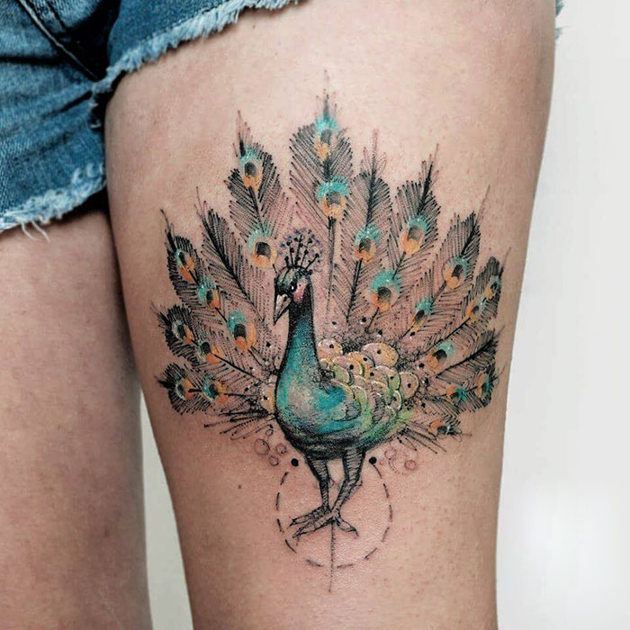 Colorful small bird tattoo of a peacock design on a thigh.